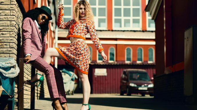 Stylish women posing in an urban alley showcasing contemporary fashion trends.