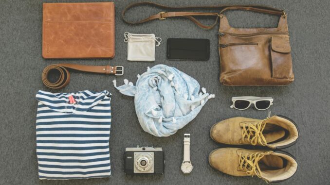 Vintage travel essentials flat lay with leather bags, shoes, camera, and clothing.