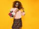 Chic woman with afro hair in a floral sweater and plaid skirt posing confidently.