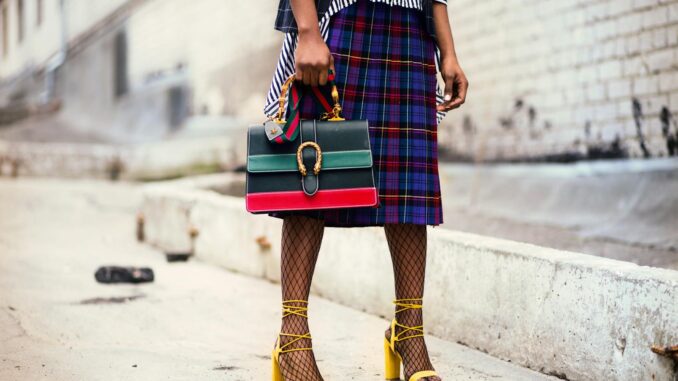 Fashion-forward outfit with plaid skirt and colorful handbag in urban setting.