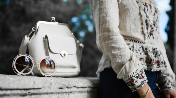 woman wearing beige and red floral top leaning on gray concrete slab with white leather bag ontop