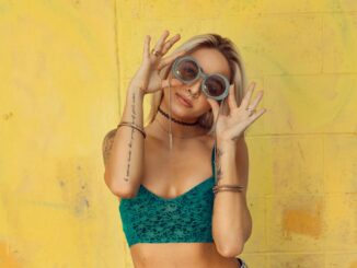 woman in blue bralette holding sunglasses putting on her eyes