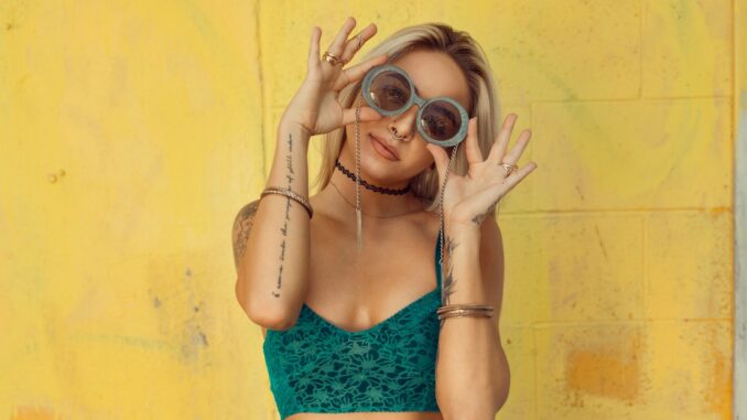 woman in blue bralette holding sunglasses putting on her eyes