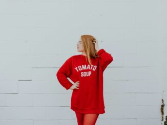 woman wearing red long-sleeved shirt standing near white painted wall