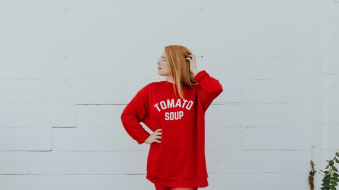 woman wearing red long-sleeved shirt standing near white painted wall